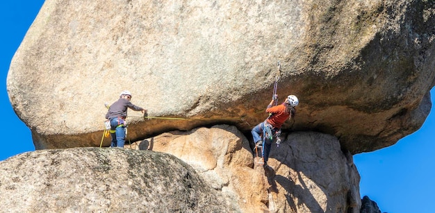 Dois jovens adultos trabalhando juntos para escalar uma parede de granito Escalada em rocha Conceito de esportes radicais