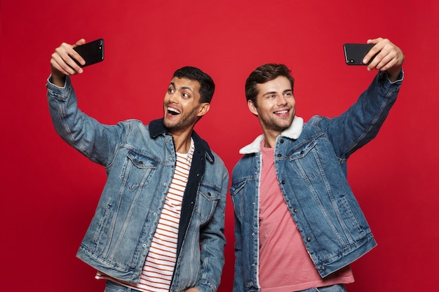 Dois jovens alegres, isolados na parede vermelha, tirando uma selfie