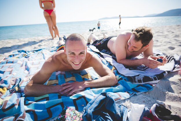 dois jovens amigos homens sorridentes deitados na praia