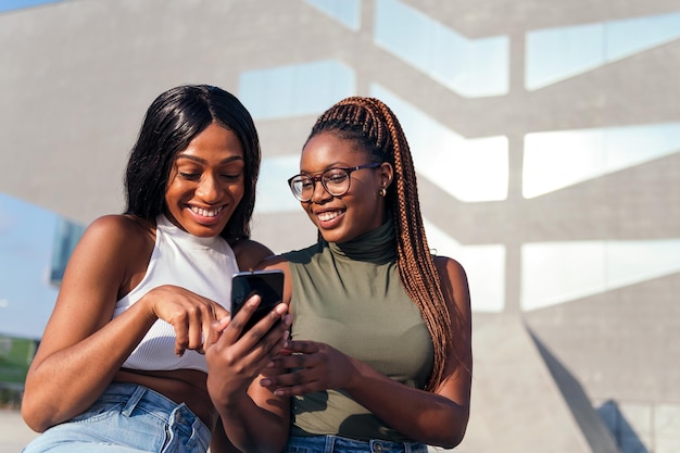 Dois jovens amigos negros sorrindo e se divertindo olhando para o celular, conceito de juventude e tecnologia de comunicação, copie o espaço para texto