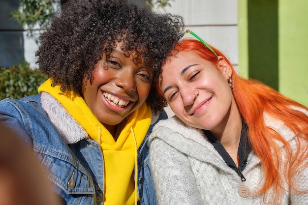 Dois jovens amigos sorrindo tirando uma selfie um cabelo afro preto e o outro cabelo laranja branco