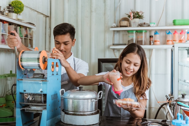 Dois jovens asiáticos e uma mulher preparando o prato em sua pequena barraca de comida de rua