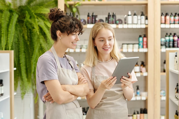 Dois jovens assistentes de loja sorridentes olhando para a tela do tablet durante o trabalho