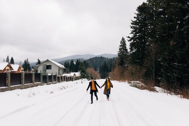 Dois jovens caminham por uma estrada cheia de neve de mãos dadas