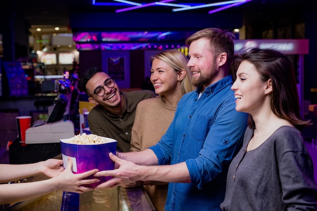 Dois jovens casais felizes comprando pipoca no caixa do cinema enquanto vão assistir a um filme juntos