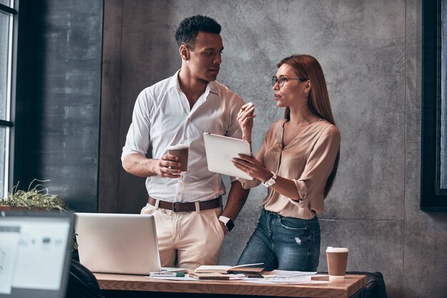 Dois jovens colegas de trabalho em roupas casuais inteligentes discutindo negócios enquanto trabalhavam no escritório