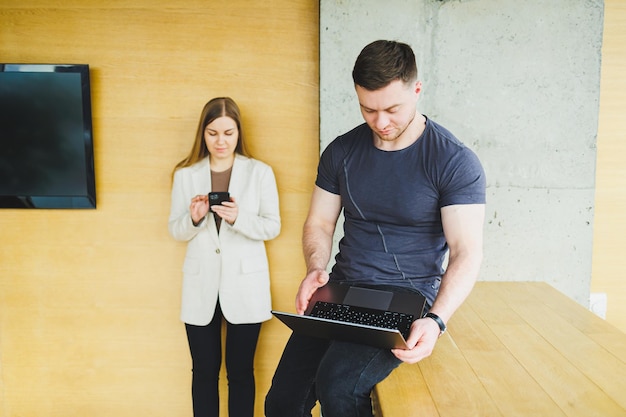 Dois jovens colegas, homem e mulher, trabalhando juntos em um espaço de trabalho moderno Dois jovens empresários sorrindo alegremente enquanto trabalham com um laptop Colegas sentam-se juntos à mesa