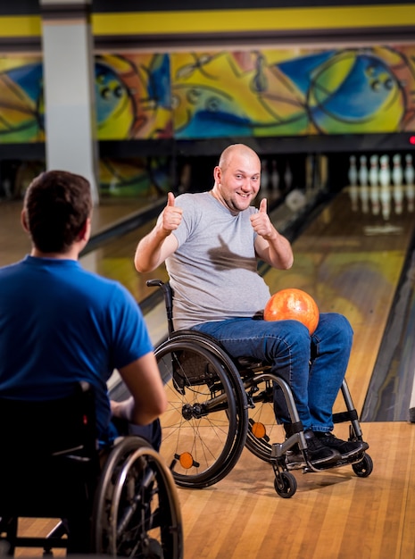 Foto dois jovens deficientes físicos em cadeiras de rodas jogando boliche no clube