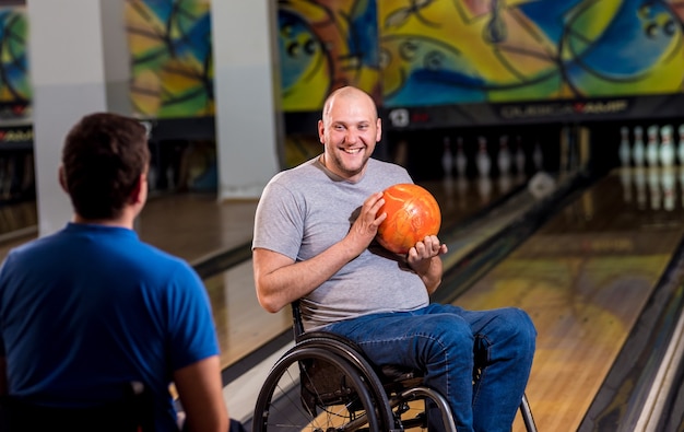 Foto dois jovens deficientes físicos em cadeiras de rodas jogando boliche no clube
