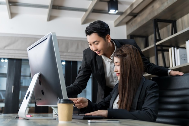 Dois jovens empresários asiáticos se encontrando e discutindo negócios olhando para o computador na mesa trabalhando juntos