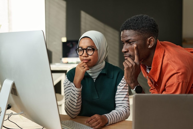 Dois jovens engenheiros de TI interculturais sérios olhando dados na tela do computador ou esperando por web p