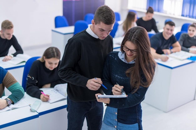 Dois jovens estudantes homem e mulher com outros trabalhando em um projeto em uma sala de aula escrevendo notas e discutindo