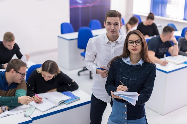 Dois jovens estudantes homem e mulher com outros trabalhando em um projeto em uma sala de aula escrevendo notas e discutindo