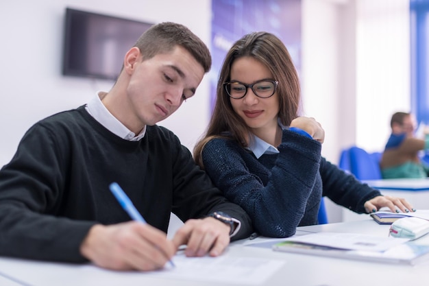 Dois jovens estudantes homem e mulher com outros trabalhando em um projeto em uma sala de aula escrevendo notas e discutindo