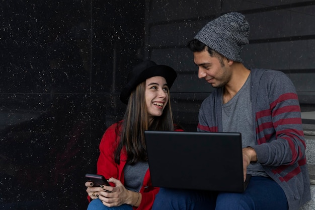 Dois jovens irmãos latino-americanos sentados nas escadas com laptop e celular