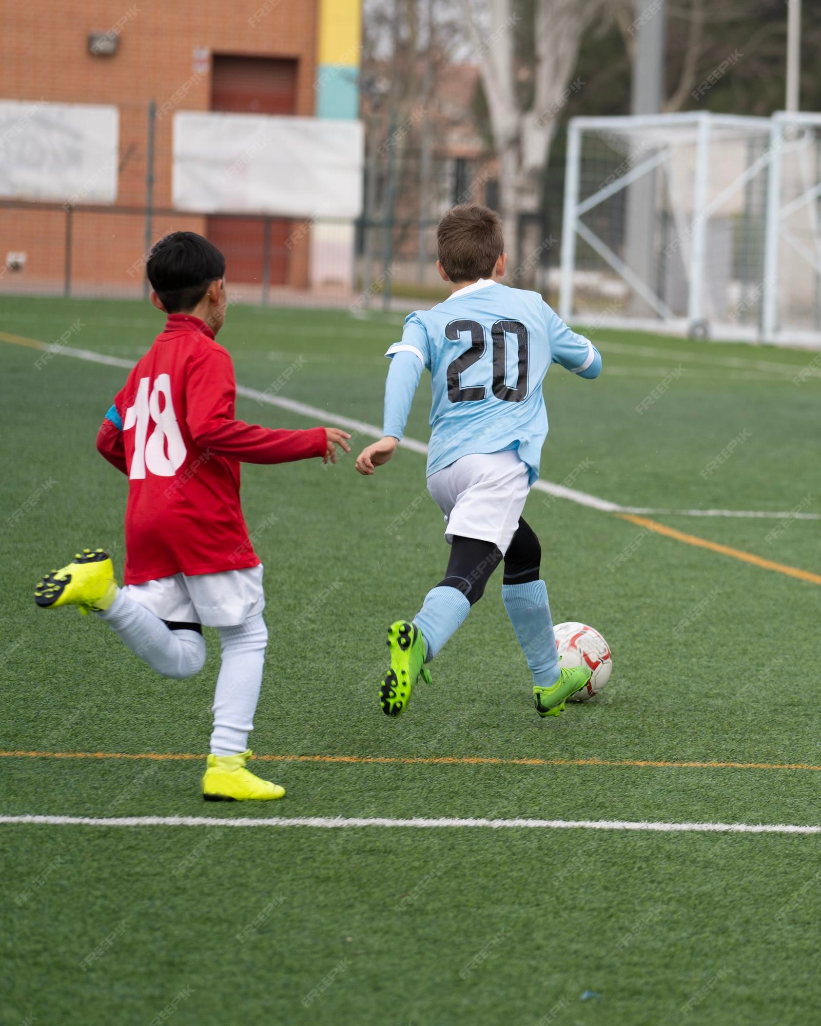 Dois Jogadores De Futebol Chutando Bola De Futebol Em Um Jogo. Meninos Da  Escola Jogam Competição Esportiva. Duas Crianças Multirraciais Jogando  Partida De Futebol. Crianças Em Uniformes De Futebol Verde E Azul