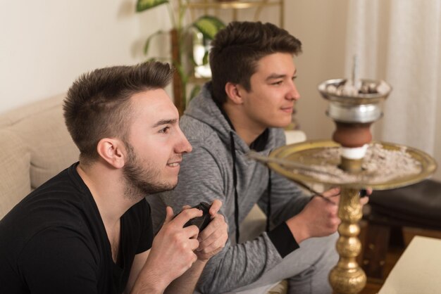Dois jovens jogadores sentados juntos no sofá e jogando videogame em casa
