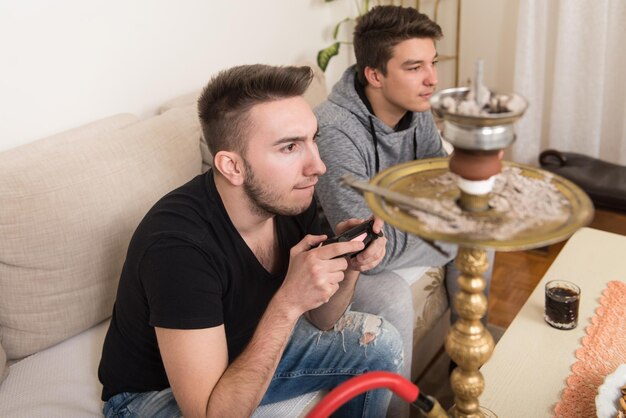 Dois jovens jogadores sentados juntos no sofá e jogando videogame em casa