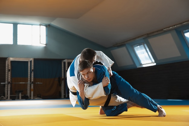 Dois jovens judocas de quimono treinando artes marciais no ginásio