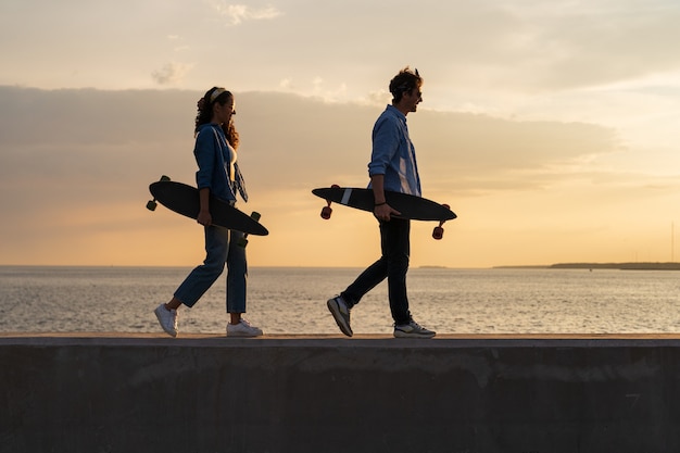 Dois jovens longboarders caminham pela beira-mar carregando skate no estilo de vida e conceito de liberdade do sol