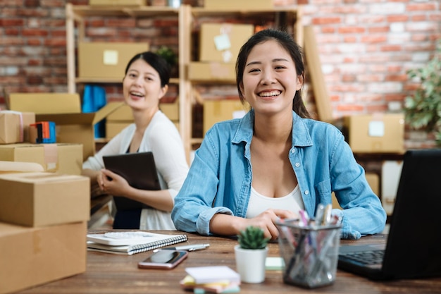 dois jovens melhores parceiros de trabalho em equipe iniciam uma loja online de pequenas empresas no escritório. colegas de senhoras bonitas que trabalham no armazém olhando câmera de rosto sorrindo alegre feliz sentado na mesa de trabalho.