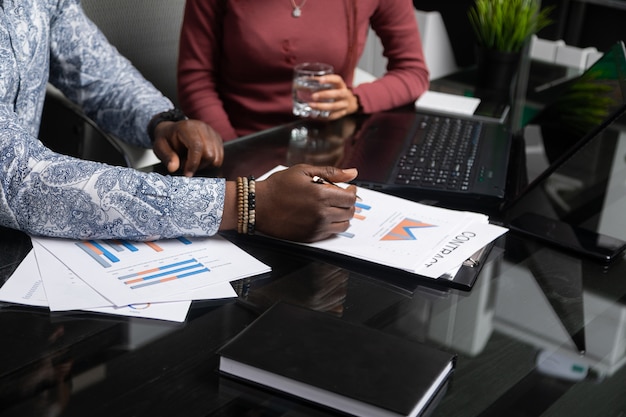 Dois jovens negros discutem seus negócios usando diagramas sentados à mesa no escritório