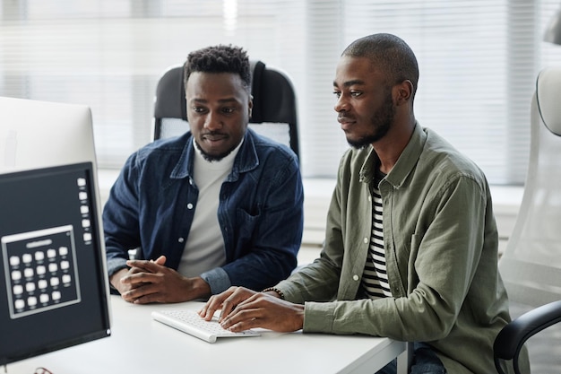 Dois jovens programadores de diversidade contemporânea em roupas casuais inserindo dados no computador enquanto estão sentados à mesa na reunião