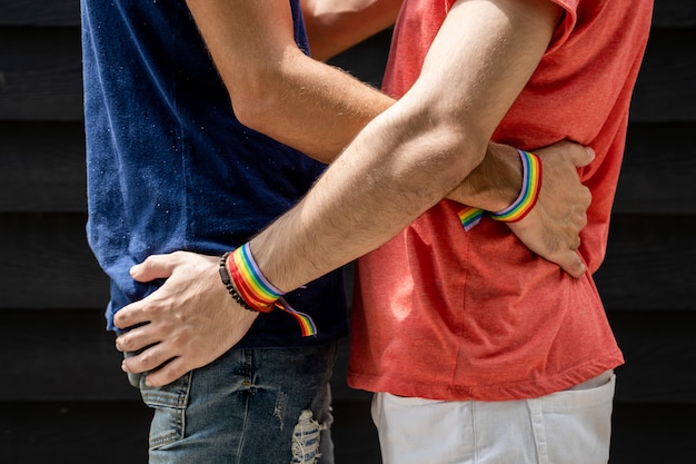 Dois jovens se abraçando na cintura com pulseiras com a bandeira lgtb do lado de fora