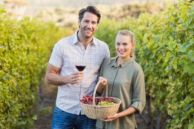 Dois jovens vinhedos felizes segurando uma cesta de uvas e um copo de vinho