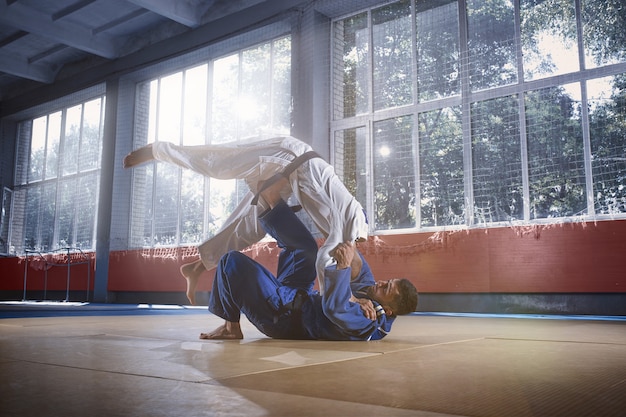 Dois judocas demonstrando habilidade técnica enquanto praticavam artes marciais em um clube de luta. os dois são homens uniformizados. luta, caratê, treinamento, artes, atleta, conceito de competição