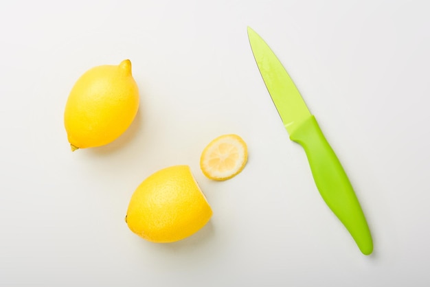 Dois limões cítricos amarelos com faca de frutas verdes na mesa branca preparada para cozinhar limonada