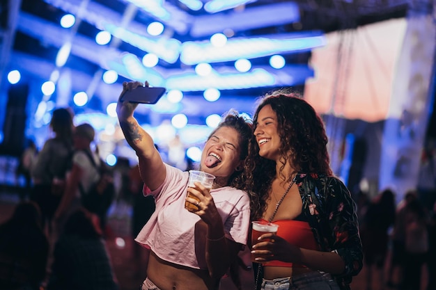 Dois lindos amigos tirando selfie com um samrtphone em um festival de música