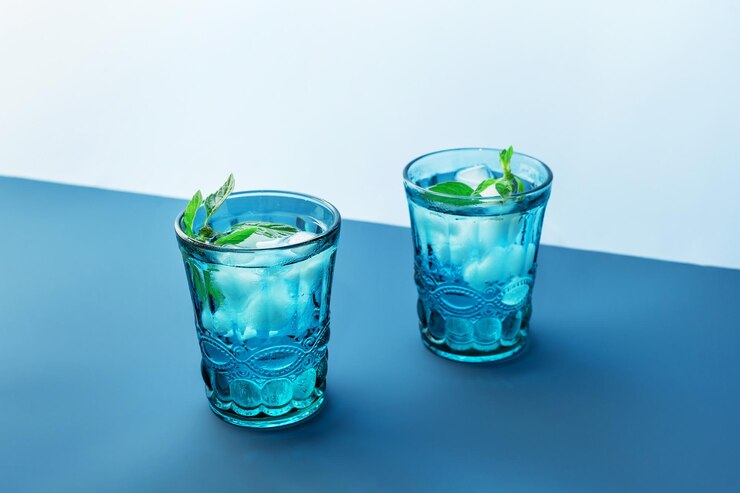 Foto dois lindos copos azuis vintage com bebida gelada e cubos de gelo com folhas de hortelã verde fresca em fundo azul profundo e azul claro pano de fundo para seu projeto