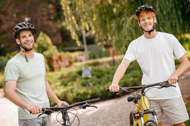 Dois lindos e sorridentes jovens ciclistas caucasianos com capacetes de segurança posando para a câmera