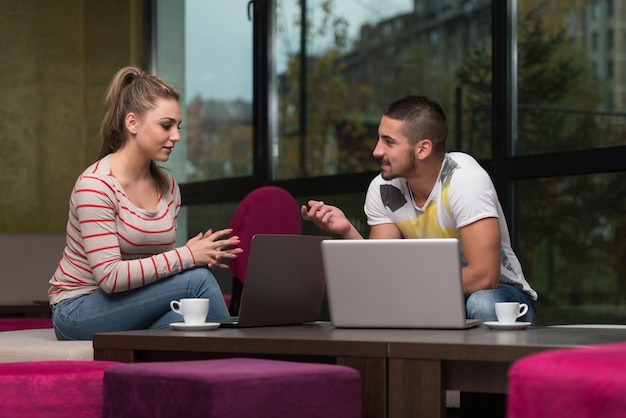 Dois lindos estudantes bebendo e se divertindo com o laptop na cafeteria