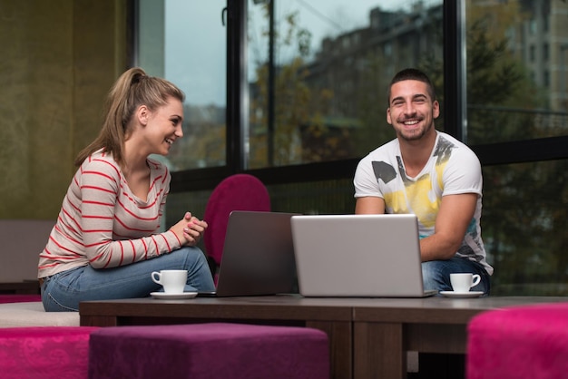 Dois lindos estudantes bebendo e se divertindo com o laptop na cafeteria