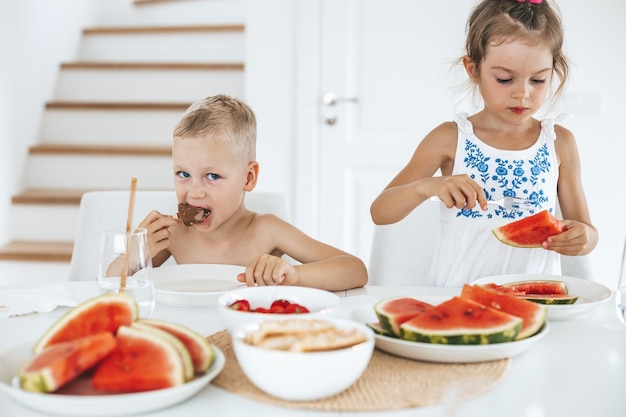 Dois lindos filhos em idade pré-escolar comendo melancia fresca e suculenta e sorvete em casa