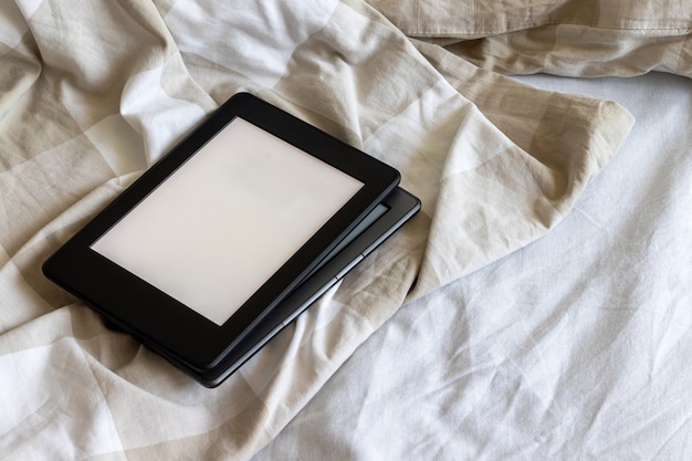 Dois livros eletrônicos modernos com telas vazias em branco em uma cama branca e bege. Comprimidos de maquete um em cima do outro na cama