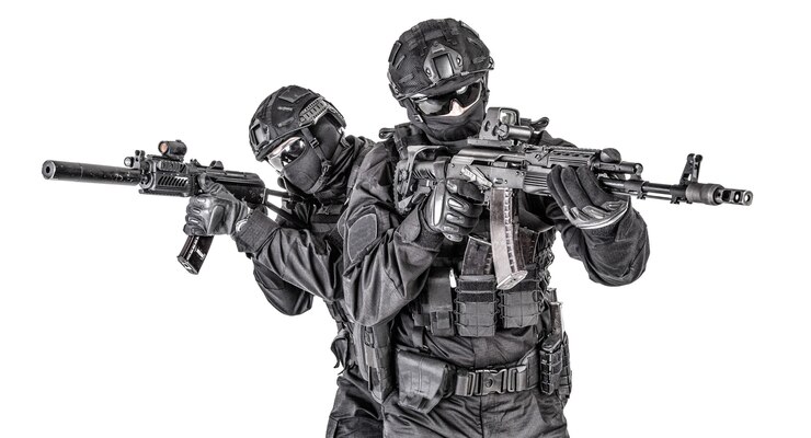 Foto dois lutadores da swat, membros do grupo tático de operações especiais da polícia em uniforme preto e capacete, armados com rifles de assalto avançando um atrás de outro tiro em estúdio isolado no fundo branco