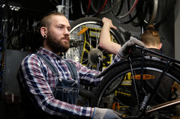 Dois machos elegantes bonitos trabalhando com uma bicicleta em uma oficina. Os trabalhadores reparam e montam a bicicleta em uma oficina.