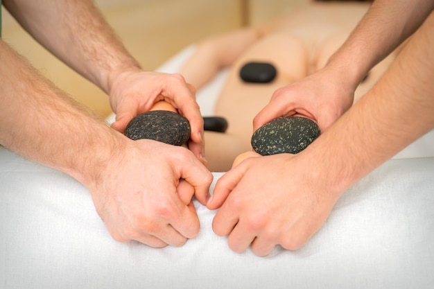 Dois massagistas fazem massagem nos pés com pedra quente a quatro mãos no spa.