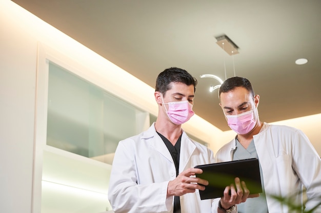 Dois médicos com máscaras olhando para a tela do tablet em uma clínica ginecológica, odontológica ou estética. conceito médico.