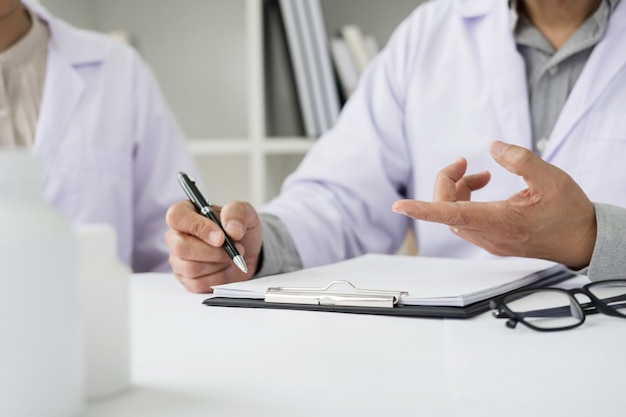 Foto dois médicos discutindo notas de pacientes em um escritório apontando para uma área de transferência com papelada, pois fazem um diagnóstico ou decidem o tratamento