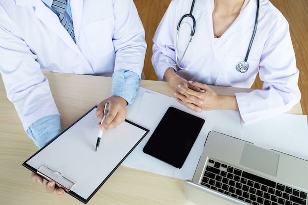 Foto dois médicos discutindo notas de pacientes em um escritório apontando para uma área de transferência com papelada, pois fazem um diagnóstico ou decidem o tratamento