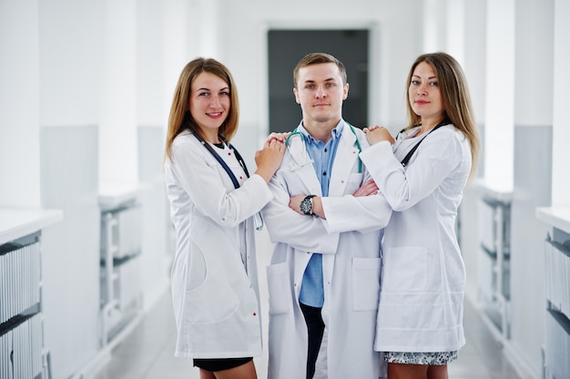 Dois médicos femininos bonitos e um homem de jaleco branco posando no hospital com estetoscópio.