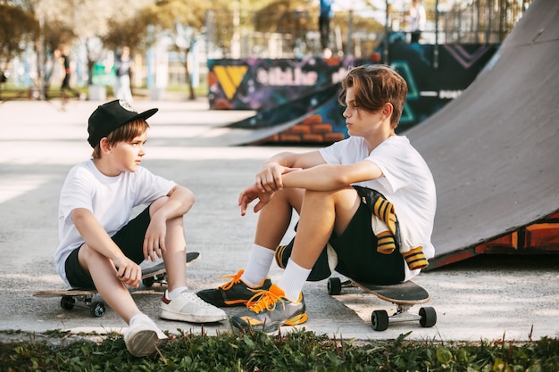 Dois melhores amigos em um parque de skate. Amigos sentam-se em patins no parque, conversando e sorrindo