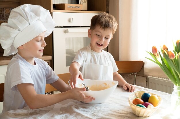 dois meninos alegres e felizes fazendo massa para o bolo de páscoa em casa na cozinha