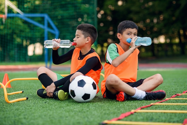 Dois meninos com uniformes de futebol bebendo água doce.