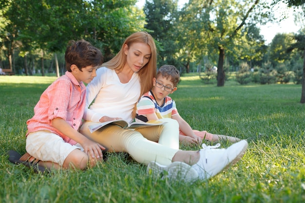 Dois meninos de escola lendo um livro com a professora ao ar livre no parque