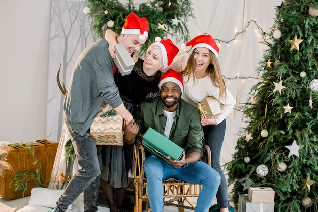 Dois meninos e duas meninas comemorando o natal em um ambiente aconchegante e decorado, segurando caixas de presente